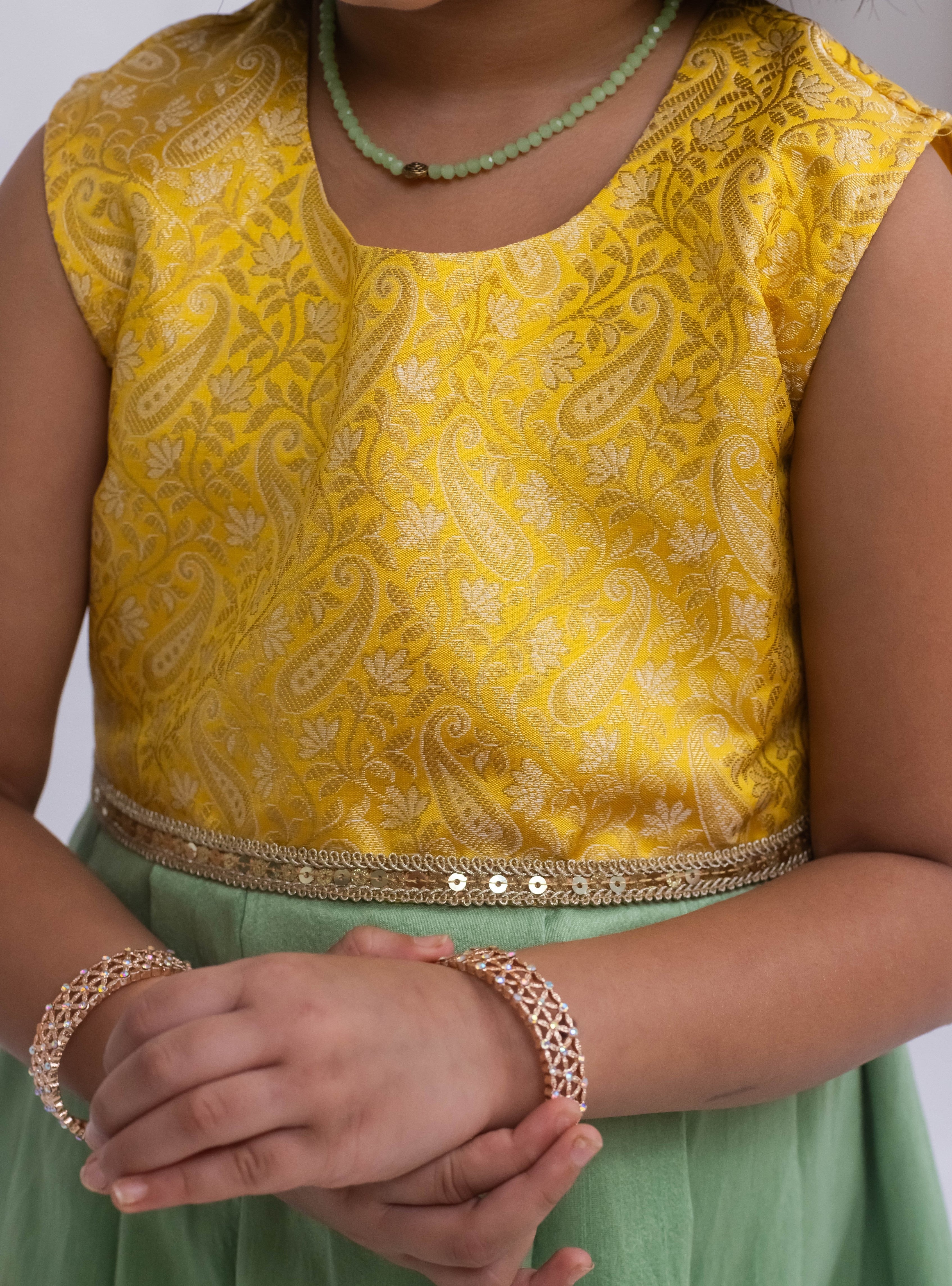 Introducing our latest product: a stunning yellow banarasi brocade yoke paired with a mint green raw silk pleated dress, complete with a delicate sequined lace waist detailing, designed specifically for girls. With its intricate craftsmanship and elegant color combination, this dress is sure to make a statement. Don't miss out on this unique addition to our collection!