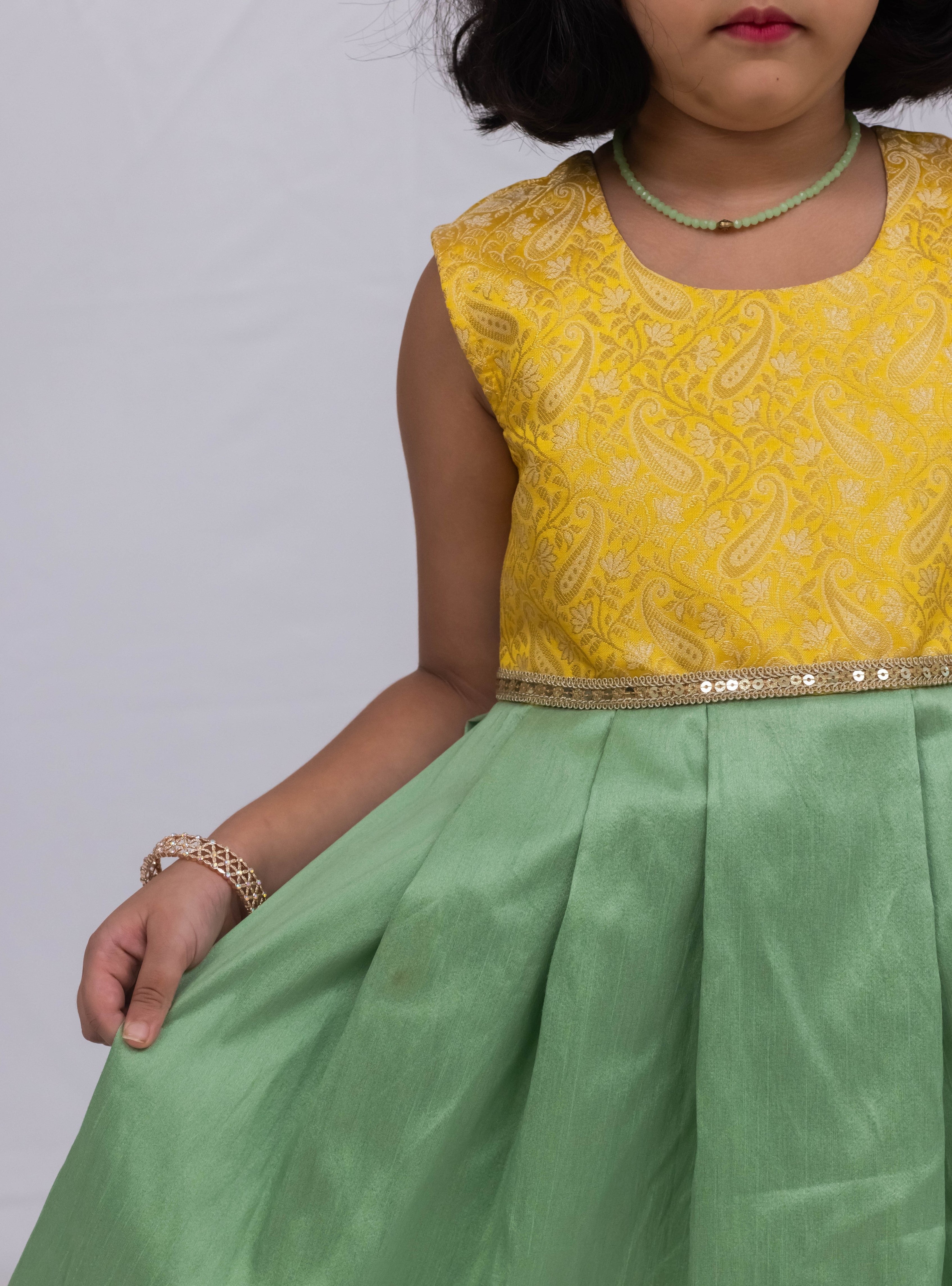 Introducing our latest product: a stunning yellow banarasi brocade yoke paired with a mint green raw silk pleated dress, complete with a delicate sequined lace waist detailing, designed specifically for girls. With its intricate craftsmanship and elegant color combination, this dress is sure to make a statement. Don't miss out on this unique addition to our collection!