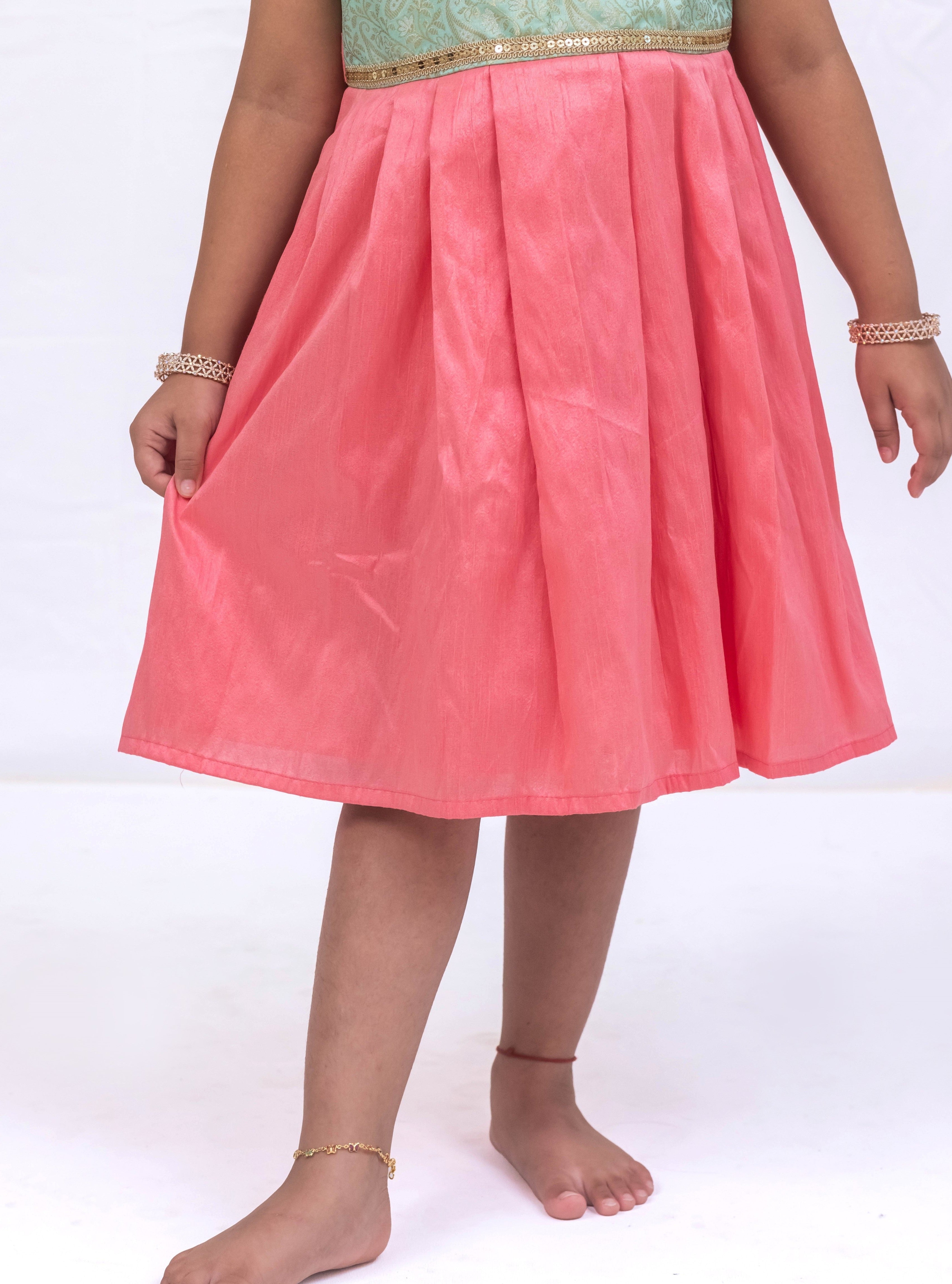 Introducing our latest product: a stunning Pista Green banarasi brocade yoke paired with a Rose Pink raw silk pleated dress, complete with a delicate sequined lace waist detailing, designed specifically for girls. With its intricate craftsmanship and elegant color combination, this dress is sure to make a statement. Don't miss out on this unique addition to our collection!