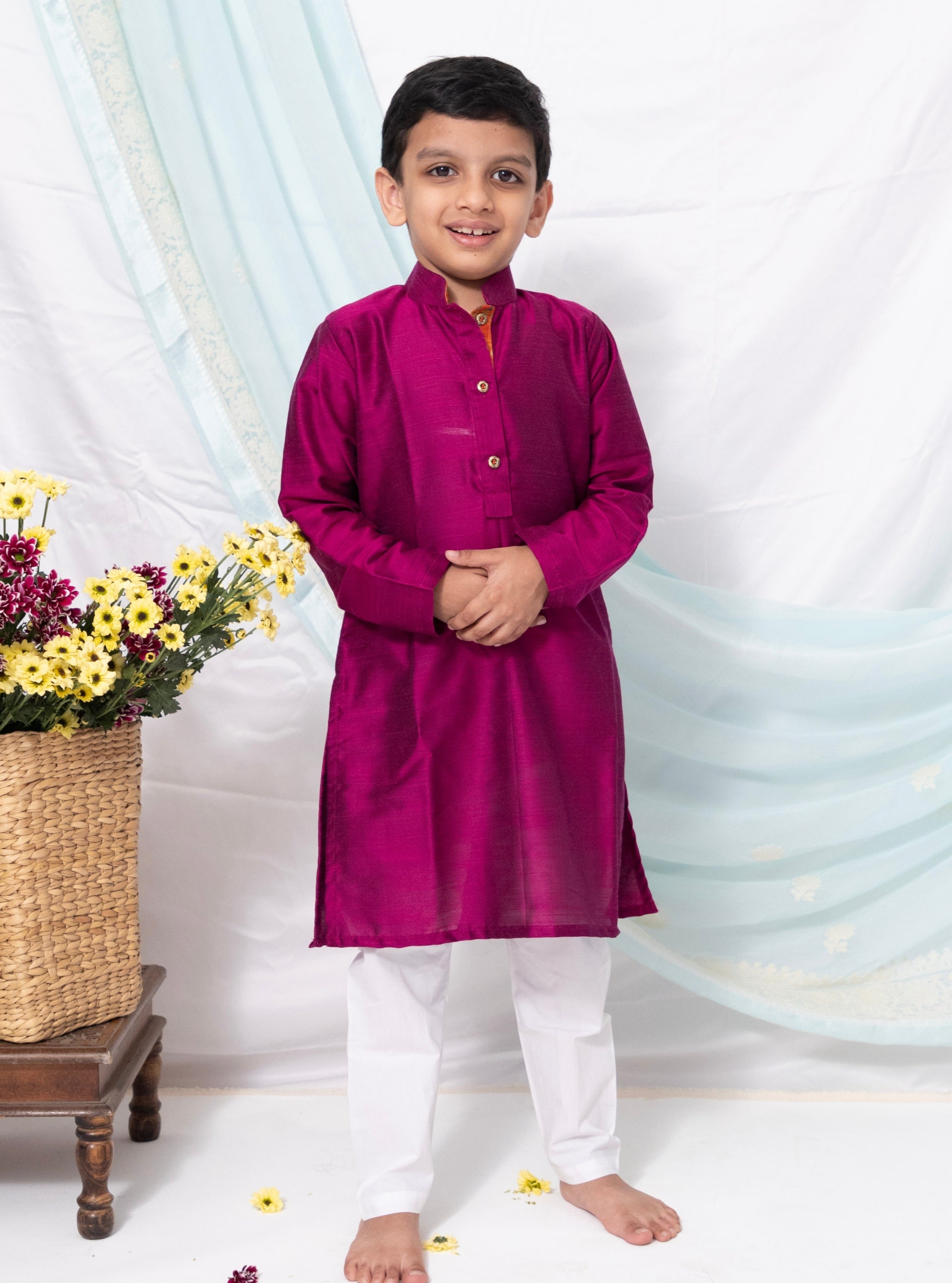 Enhance your traditional ensemble with this Magenta cotton silk kurta for Boys. Featuring a stand collar, orange placket detailing, and golden buttons, it can be paired with salwar or jeans for a stylish and comfortable look.