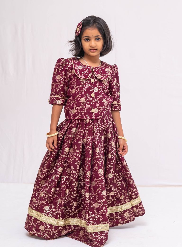 This Dark Plum banaras brocade ghagra is complemented by a Peterpan collared mutton sleeved choli.Let your princess be as comfortable as in her casuals with carefully designed & crafted Comfort Ethnic Wear by Soyara Ethnics.Keep her fashion quotient high with timeless patterns, vibrant combinations and royal textiles.