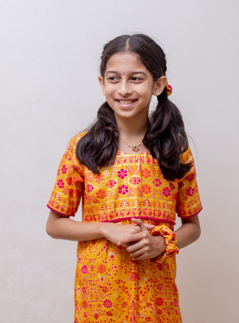 Yellow soft silk banaras brocade kurti with yoke pattern embellished with contrast pompom lace for Girls.Let your princess be as comfortable as in her casuals with carefully designed & crafted Comfort Ethnic Wear by Soyara Ethnics.Keep her fashion quotient high with timeless patterns, vibrant combinations and royal textiles.