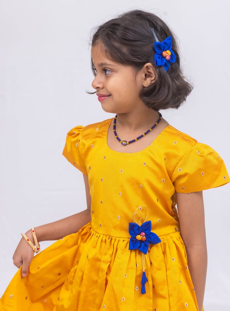 This stunning dress is made of yellow taffeta silk and features elegant puff sleeves. The dress also includes a delicate handmade fabric flower brooch, adding a touch of sophistication. A matching blue hair clip is included for a coordinated look.
