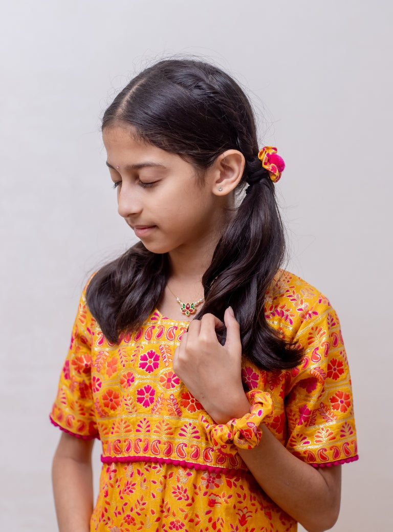 Yellow soft silk banaras brocade kurti with yoke pattern embellished with contrast pompom lace for Girls.Let your princess be as comfortable as in her casuals with carefully designed & crafted Comfort Ethnic Wear by Soyara Ethnics.Keep her fashion quotient high with timeless patterns, vibrant combinations and royal textiles.
