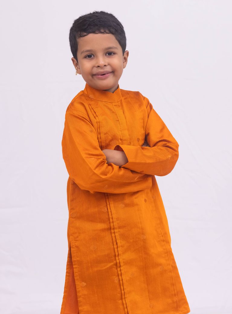 This Rust colored kurta for boys features a knife pleated design crafted from raw silk. Adorned with jari buttas, it boasts a stand collar and front placket opening for a sophisticated touch. The cotton lining on the inside ensures comfort and quality.