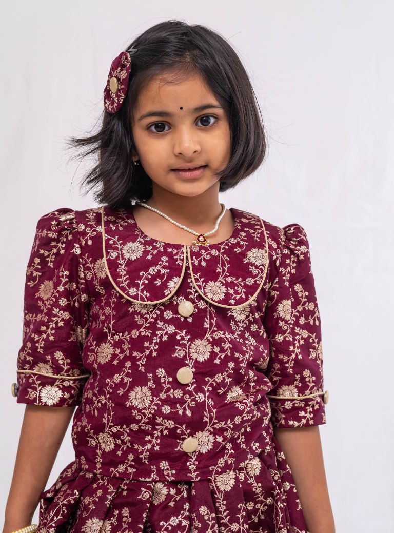 This Dark Plum banaras brocade ghagra is complemented by a Peterpan collared mutton sleeved choli.Let your princess be as comfortable as in her casuals with carefully designed & crafted Comfort Ethnic Wear by Soyara Ethnics.Keep her fashion quotient high with timeless patterns, vibrant combinations and royal textiles.