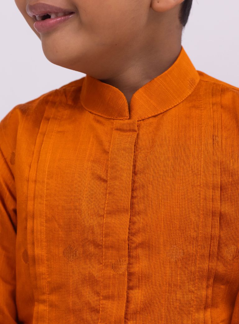 This Rust colored kurta for boys features a knife pleated design crafted from raw silk. Adorned with jari buttas, it boasts a stand collar and front placket opening for a sophisticated touch. The cotton lining on the inside ensures comfort and quality.