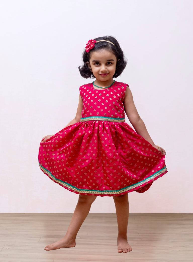 Deep pink brocade silk sleeveless flared dress with turquoise coloured sequined border for Girls.Let your princess be as comfortable as in her casuals with carefully designed and crafted Comfort Ethnic Wear by Soyara Ethnics. Keep her fashion quotient high with timeless patterns, vibrant combinations and royal textiles.
