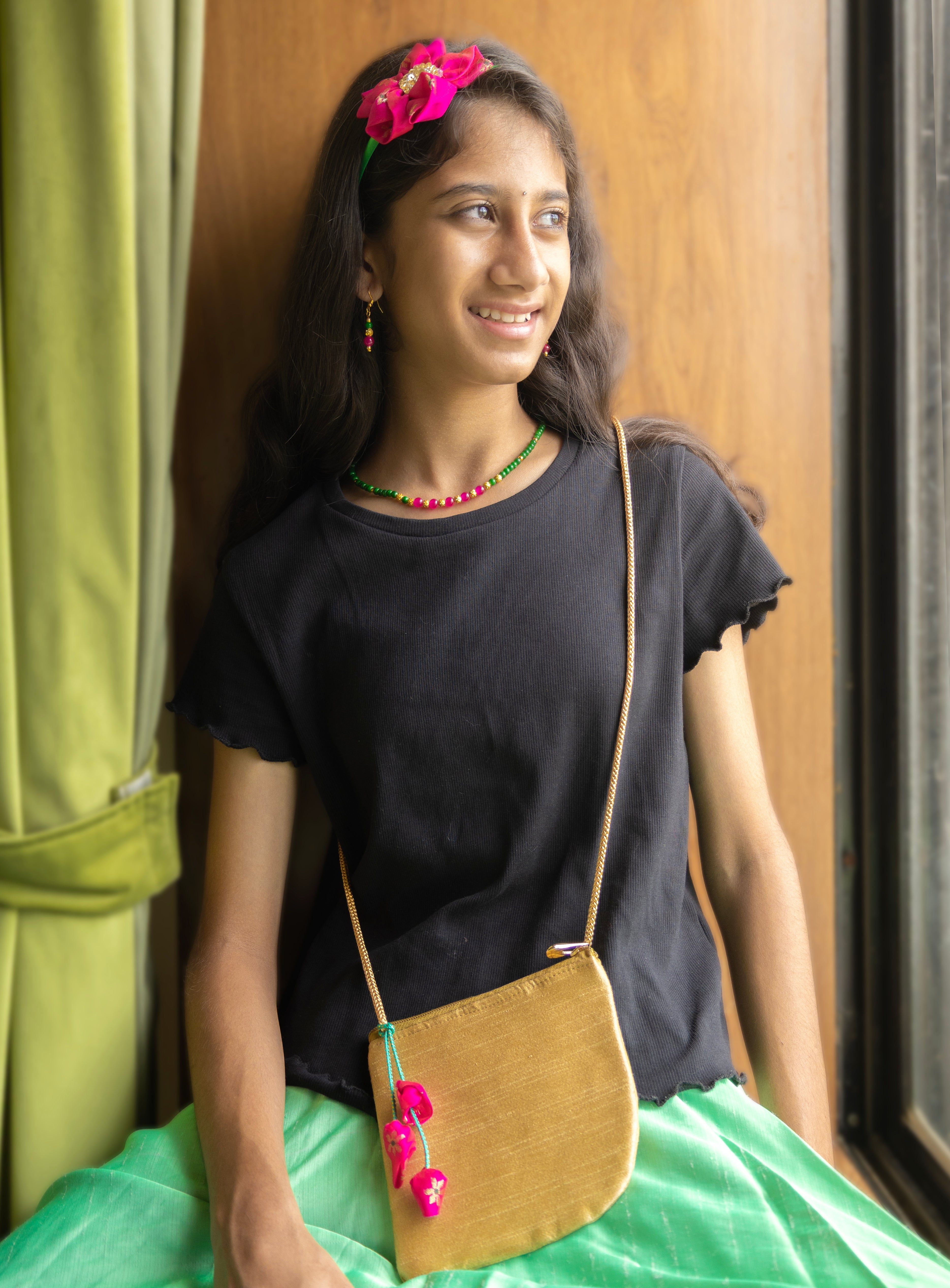 The Baby Pink and Sky Blue Purna set features a flower motif headband, necklace, earrings, and a coordinated sling purse. The necklace is crafted from high-quality glass beads with gold-plated accents. The golden raw silk sling purse is equipped with a gold-toned metal zipper for secure closure.