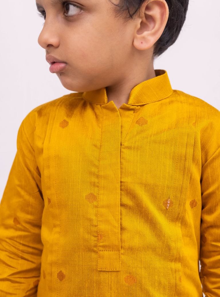 This Mustered Yellow kurta for boys features a knife pleated design crafted from raw silk. Adorned with jari buttas, it boasts a stand collar and front placket opening for a sophisticated touch. The cotton lining on the inside ensures comfort and quality.