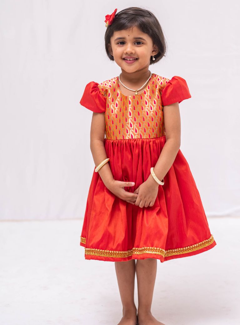 Orange banaras brocade with coral orange raw silk flared cap sleeved dress for Girls. Elevate any occasion with this unique piece.Let your princess be as comfortable as in her casuals with carefully designed and crafted Comfort Ethnic Wear by Soyara Ethnics.