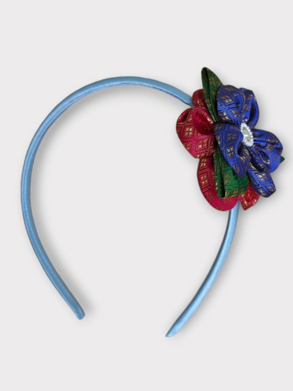 Blue brocade layered flower motif , satin wrapped plastic hairband for Girls.This blue brocade hairband features a layered flower motif and is wrapped in satin-covered plastic. It is perfect for girls aged two and up, making it a charming accessory for any outfit.