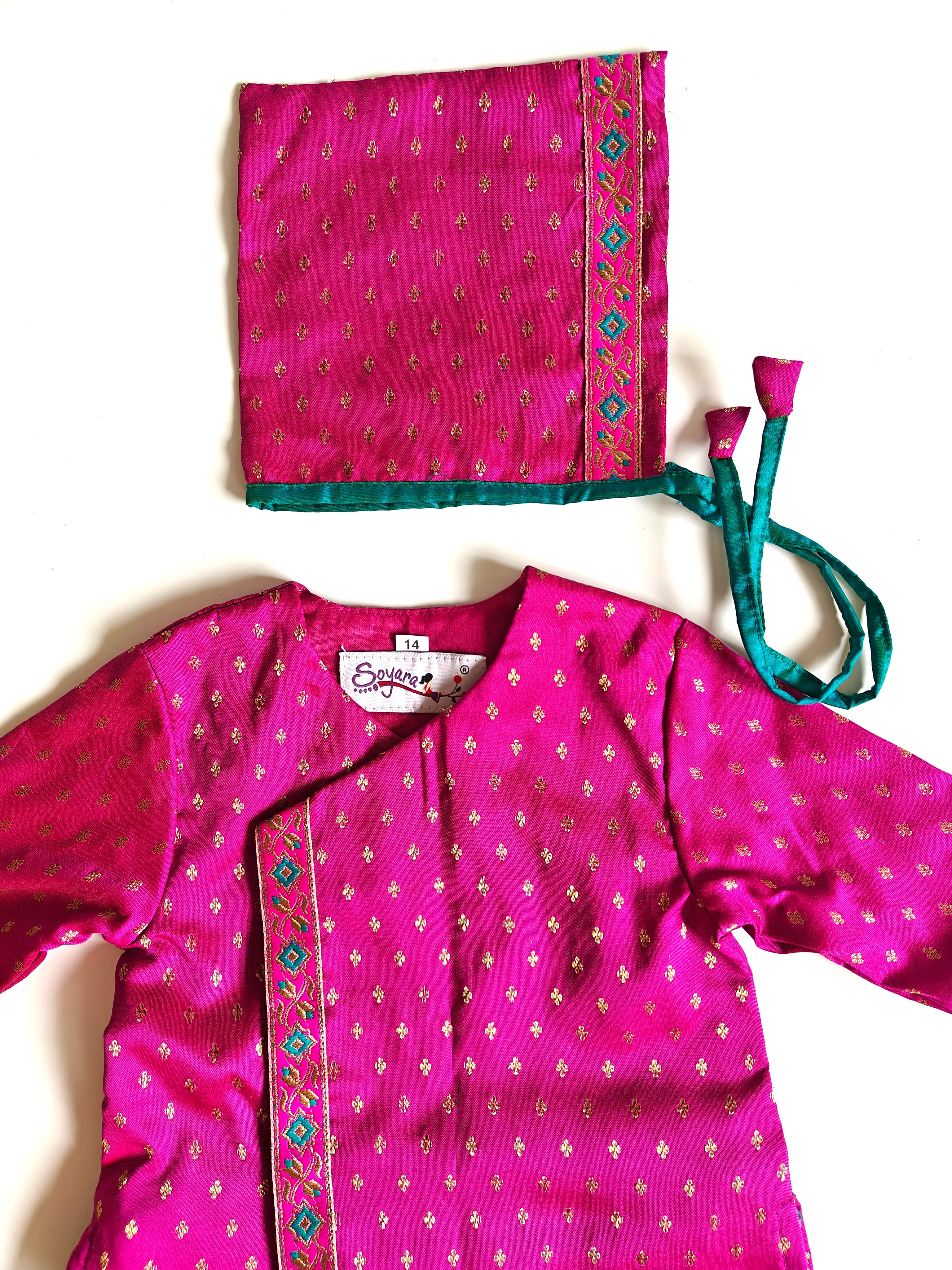 This Sharad Kurta and dhoti ensemble for baby boys features a soft brocade silk front-open kurta adorned with contrasting lace details, paired with a vibrant aqua green pooja silk dhoti. The set is completed with a matching bonnet and booties, offering a coordinated and elegant traditional outfit.