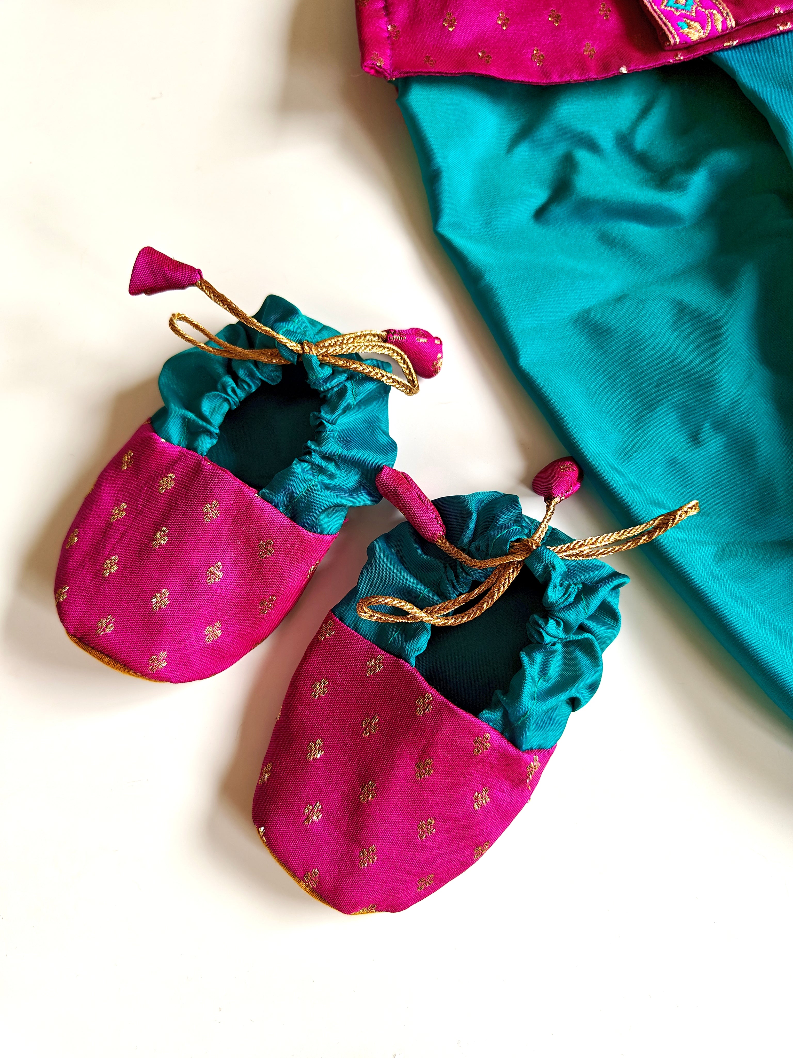 This Sharad Kurta and dhoti ensemble for baby boys features a soft brocade silk front-open kurta adorned with contrasting lace details, paired with a vibrant aqua green pooja silk dhoti. The set is completed with a matching bonnet and booties, offering a coordinated and elegant traditional outfit.