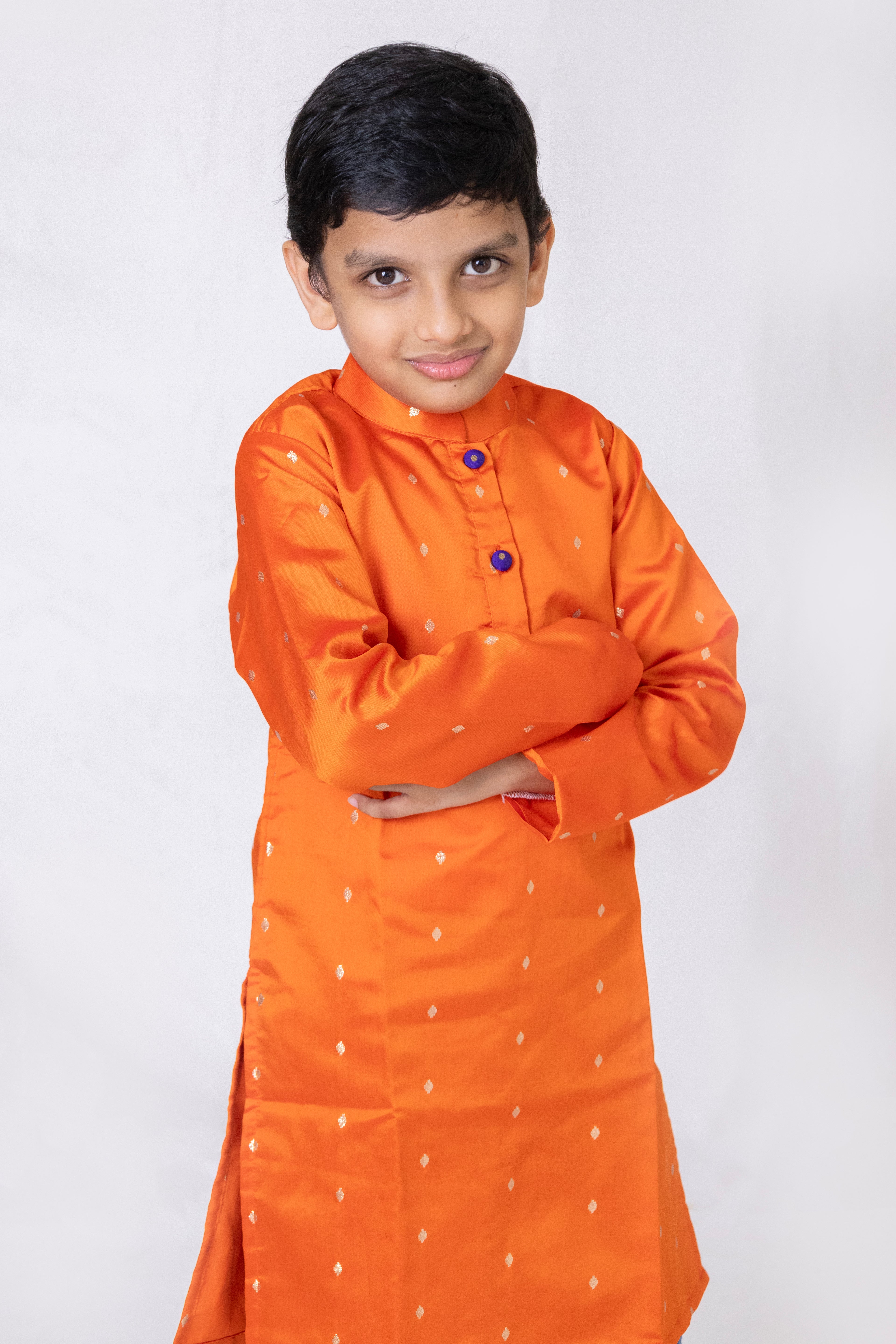 This boys' kurta features a vibrant orange taffeta silk fabric with a stand collar and purple fabric buttons. It is lined with cotton inside to ensure added comfort and premium quality.