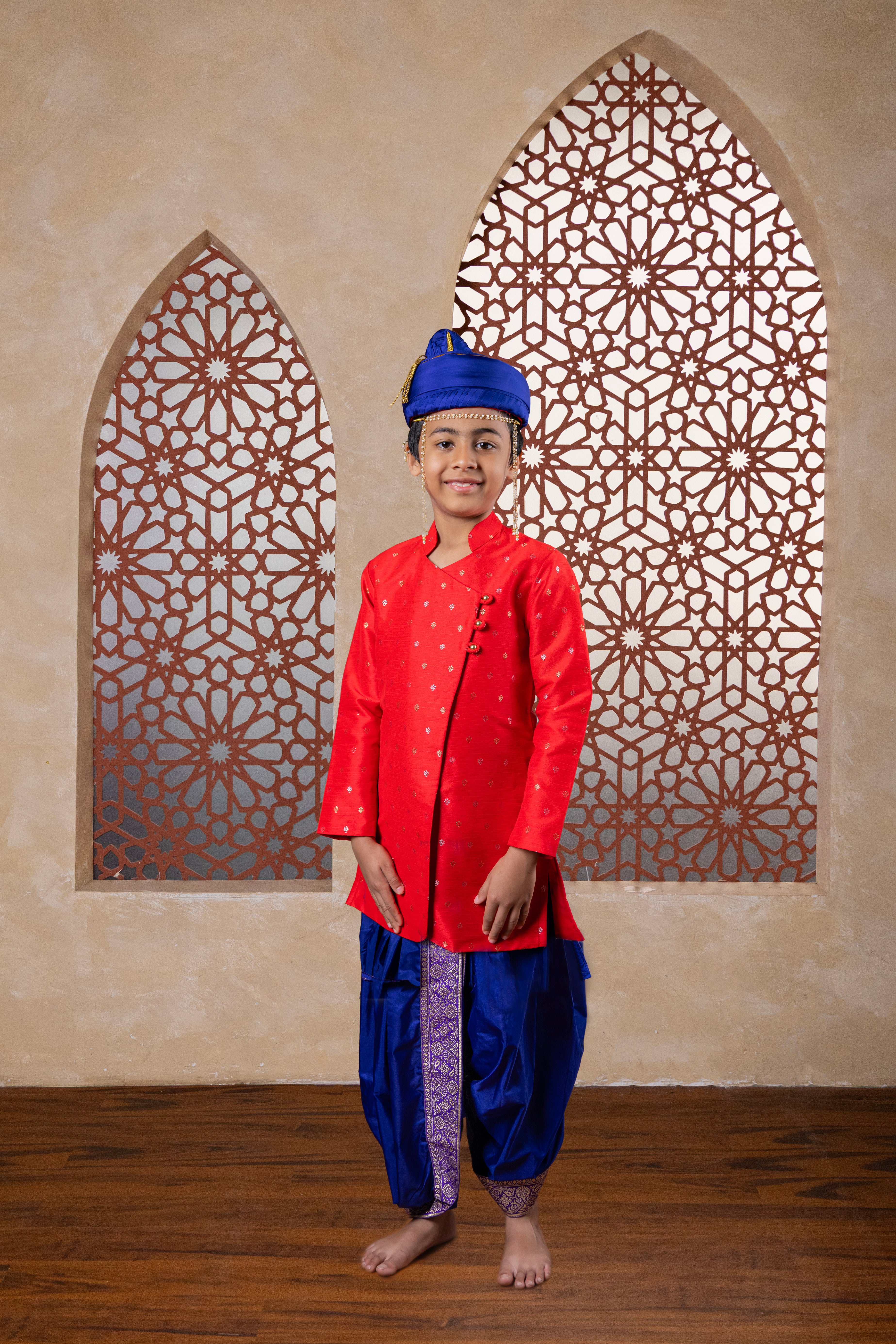This Bright Red kurta features a half stand collar and is crafted from raw silk adorned with zari motifs. It showcases an elegant overlap pattern, perfect for Batu occasions.