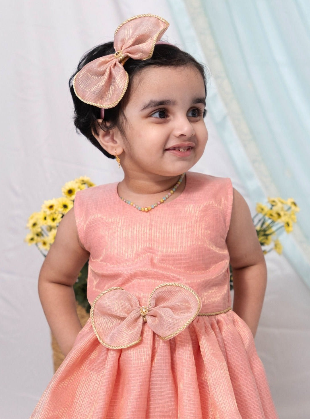 Pink tissue kotta silk sleeveless flared dress with statement embellished bow for Girl.Let your princess be as comfortable as in her casuals with carefully designed and crafted Comfort Ethnic Wear by Soyara Ethnics. Keep her fashion quotient high with timeless patterns, vibrant combinations and royal textiles.