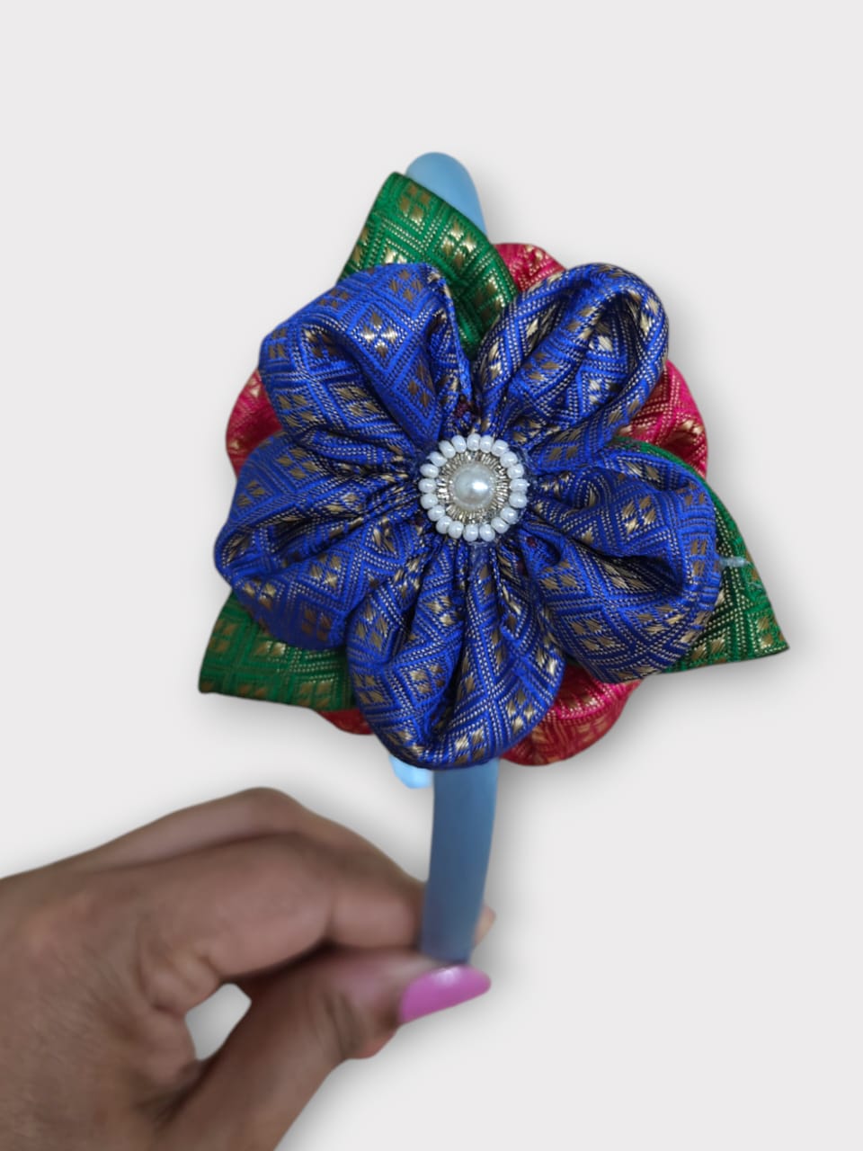 Blue brocade layered flower motif , satin wrapped plastic hairband for Girls.This blue brocade hairband features a layered flower motif and is wrapped in satin-covered plastic. It is perfect for girls aged two and up, making it a charming accessory for any outfit.