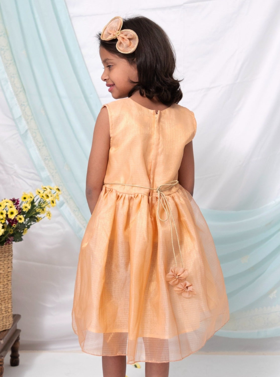 Peach tissue kotta silk sleeveless flared dress with statement embellished bow for Girl.Let your princess be as comfortable as in her casuals with carefully designed and crafted Comfort Ethnic Wear by Soyara Ethnics. Keep her fashion quotient high with timeless patterns , vibrant combinations and  royal textiles.
