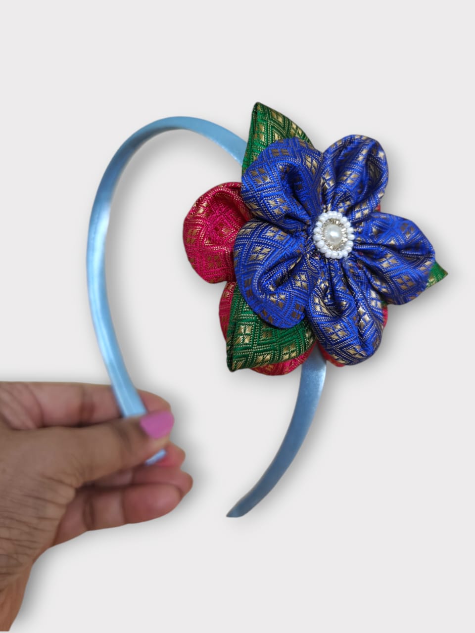 Blue brocade layered flower motif , satin wrapped plastic hairband for Girls.This blue brocade hairband features a layered flower motif and is wrapped in satin-covered plastic. It is perfect for girls aged two and up, making it a charming accessory for any outfit.