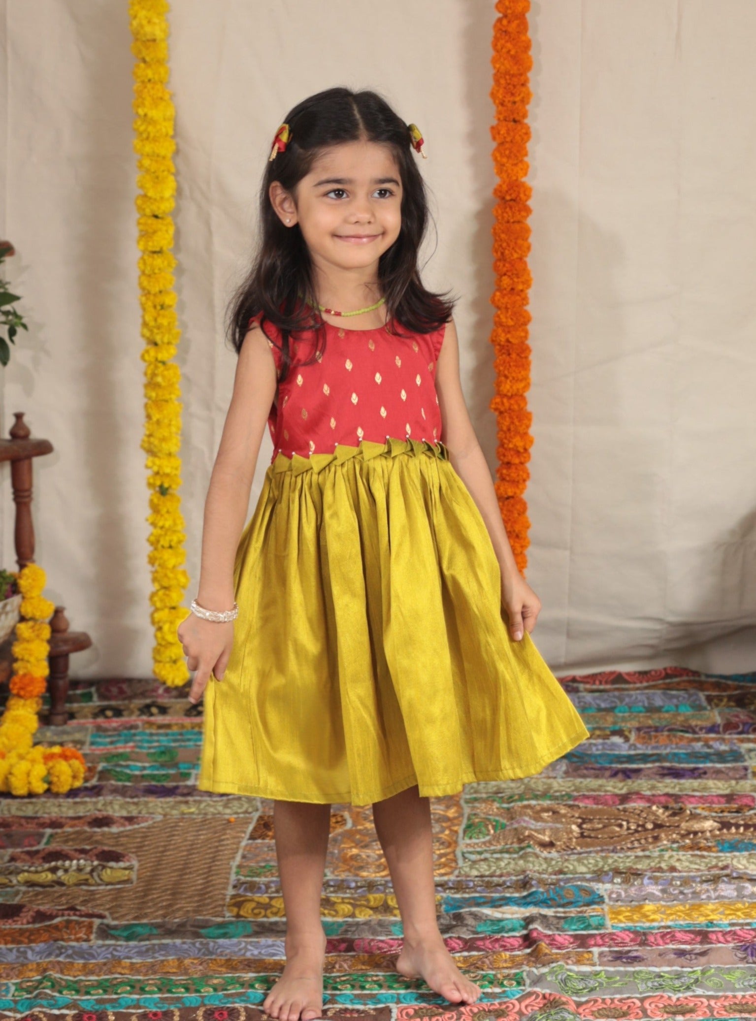 Red brocade short bodice frock with olive green raw silk bottom for girl.Let your princess be as comfortable as in her casuals with carefully designed & crafted Comfort Ethnic Wear by Soyara Ethnics.Keep her fashion quotient high with timeless patterns, vibrant combinations and royal textiles.