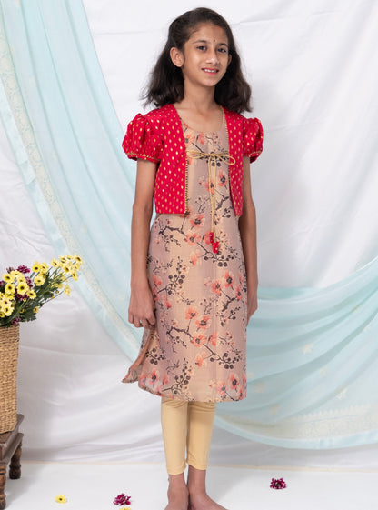 This Pastel mauve floral printed tissue kurti comes with tomato red brocade silk false shrugs. The puffed sleeves and jacket feature intricate gotta patti detailing. The kurti is adorned with charming latkans and the chord ties add a touch of fun.