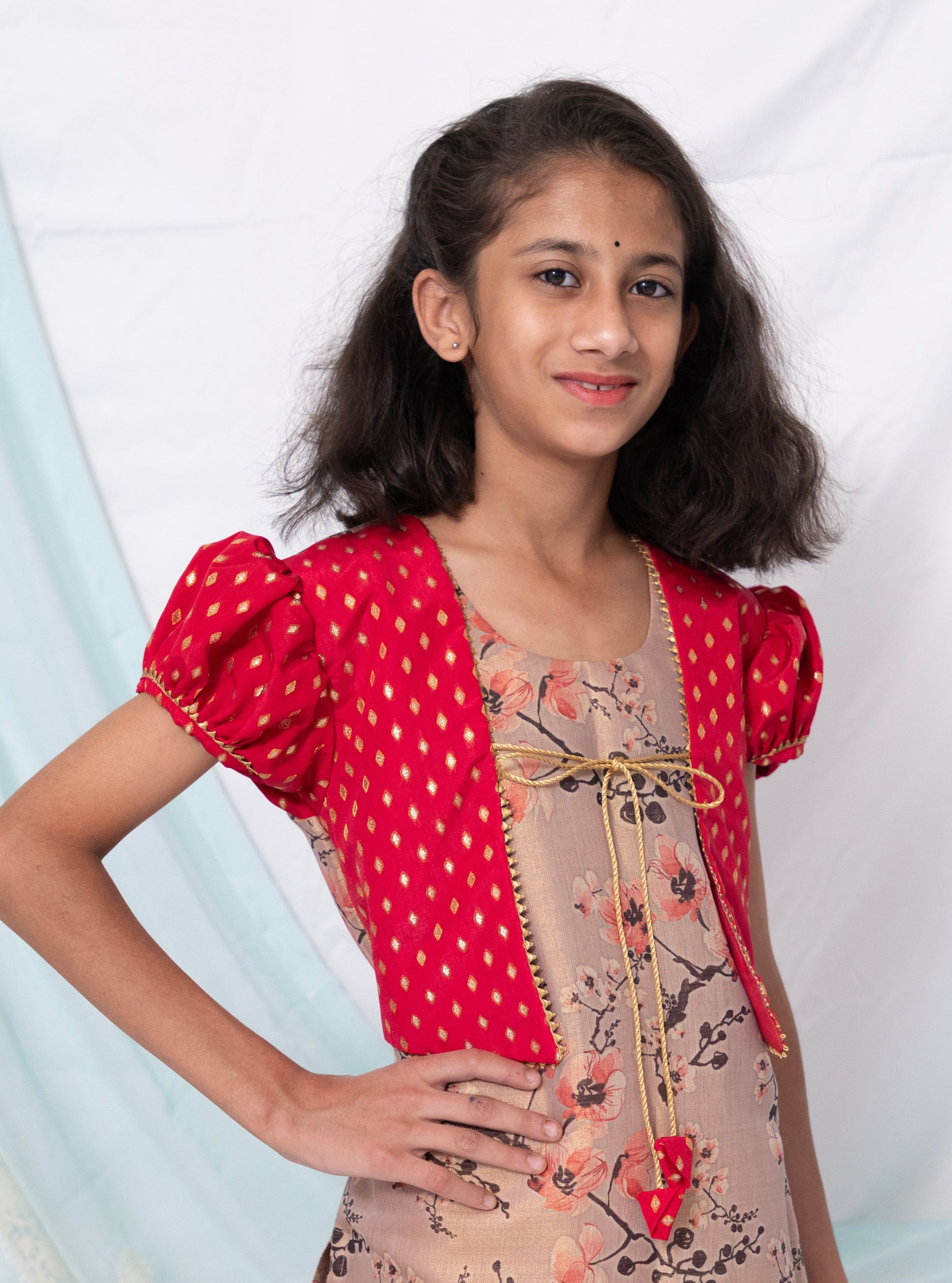 Pastel mauve coloured floral printed tissue kurti with red coloured silk false shrugs for Girls.Let your princess be as comfortable as in her casuals with carefully designed & crafted Comfort Ethnic Wear by Soyara Ethnics.Keep her fashion quotient high with timeless patterns, vibrant combinations and royal textiles.