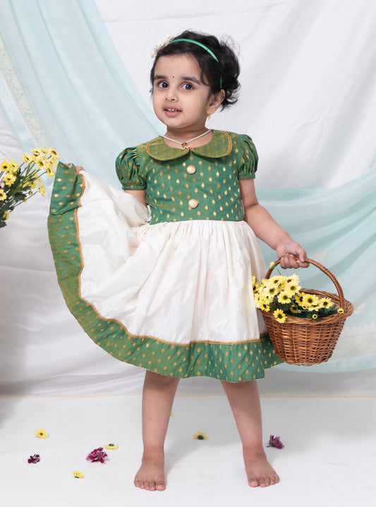 This dress features a combination of green brocade silk and ivory Mysore silk, complete with a Peter pan collar and puffed sleeves. The bodice is adorned with contrasting buttons for a touch of elegance