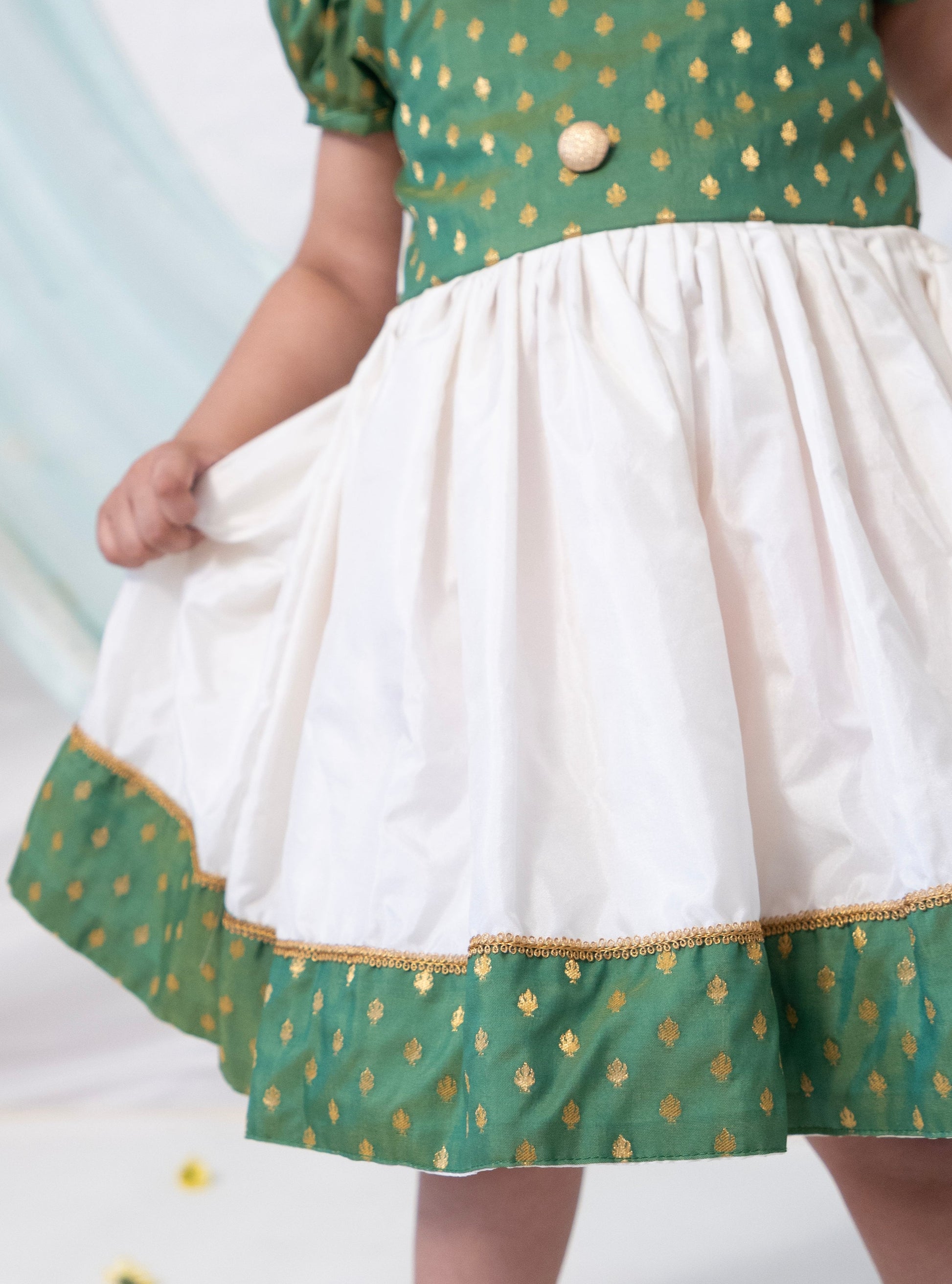 Green brocade silk and Ivory Mysore silk dress with Peter pan collar and puffed sleeves for Girl.Let your princess be as comfortable as in her casuals with carefully designed & crafted Comfort Ethnic Wear by Soyara Ethnics.Keep her fashion quotient high with timeless patterns, vibrant combinations and royal textiles.