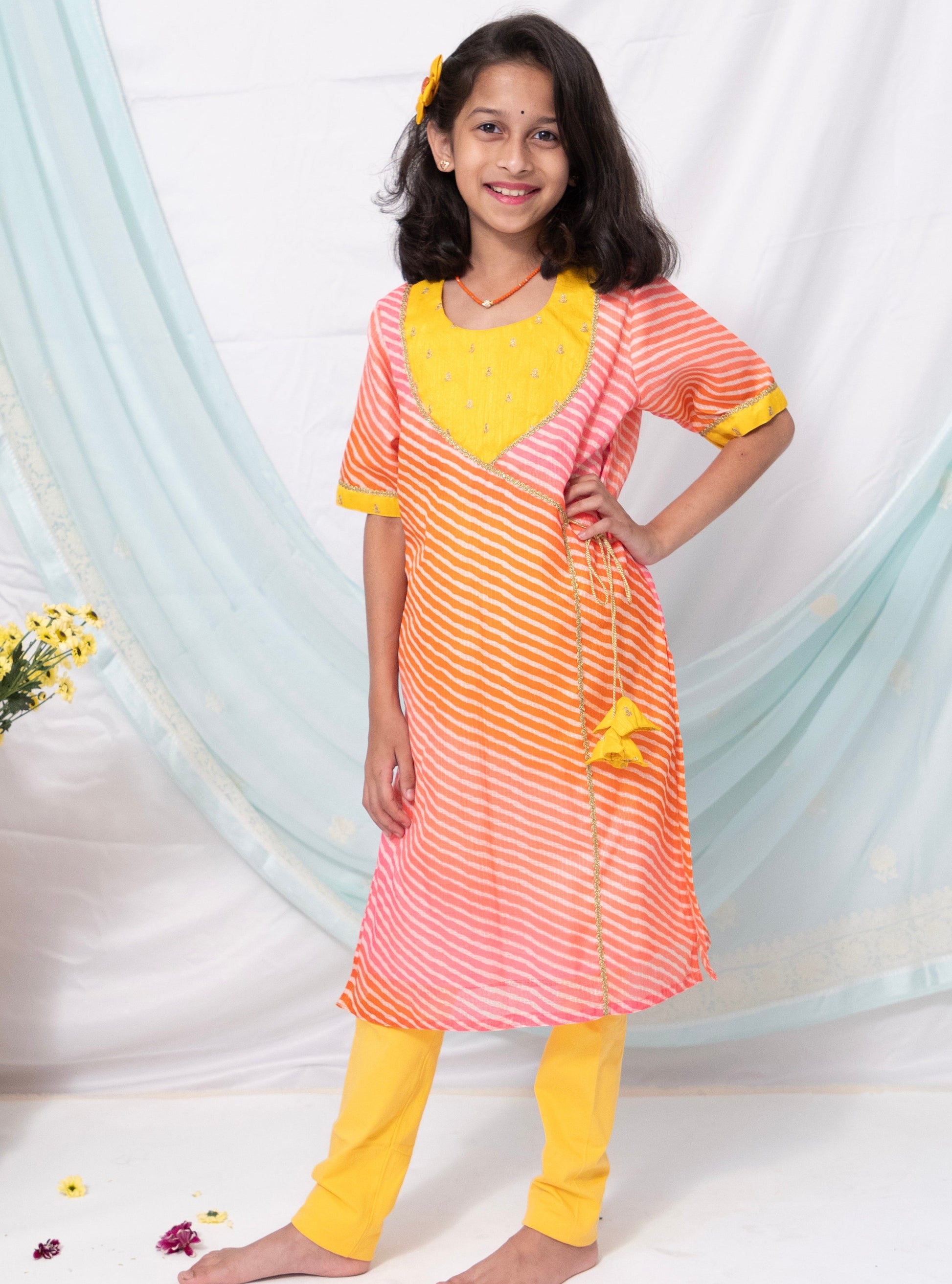 Pink and orange leheriya kotta chanderi kurti with yellow raw silk sequined yoke and flower shaped latkans is the perfect choice for any occasion, especially when paired with yellow leggings . Its elbow length sleeves with yellow highlights add a touch of elegance to the overall look.