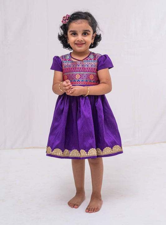 Purple banaras brocade with Purple raw silk flared cap sleeved dress for Girls. Elevate any occasion with this unique piece.Let your princess be as comfortable as in her casuals with carefully designed and crafted Comfort Ethnic Wear by Soyara Ethnics.
