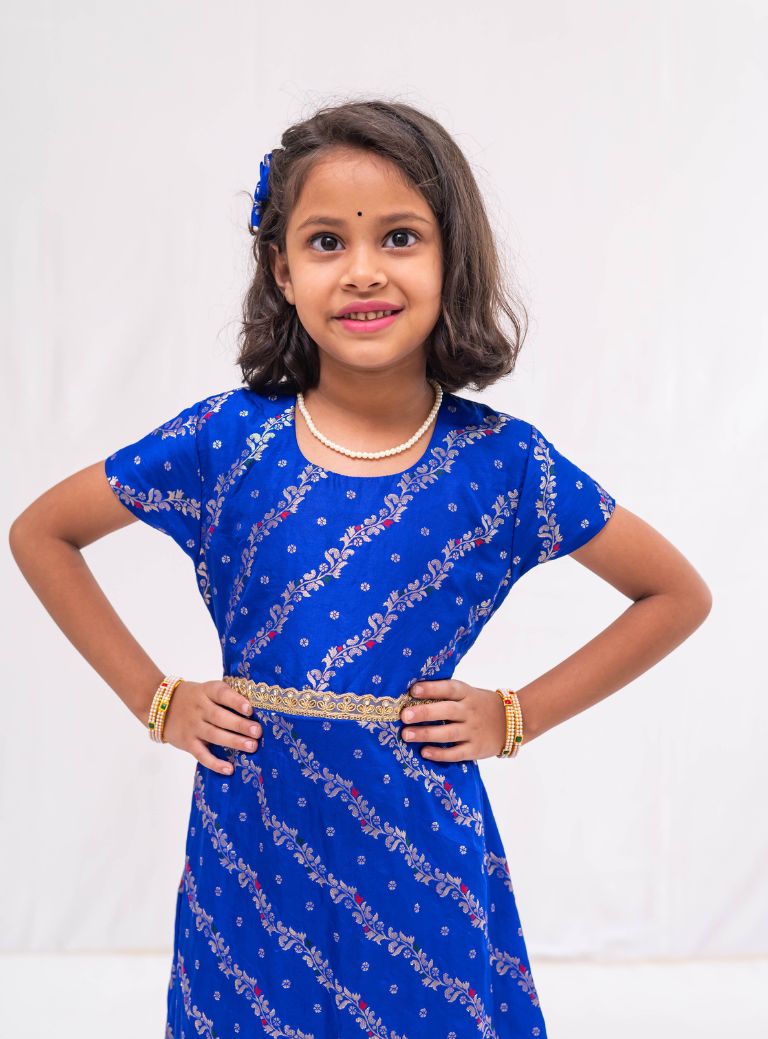 Ink blue banaras satin brocade silk gown with cap sleeves and ruffled flare for Girls.Let your princess be as comfortable as in her casuals with carefully designed & crafted Comfort Ethnic Wear by Soyara Ethnics.Keep her fashion quotient high with timeless patterns, vibrant combinations and royal textiles.
