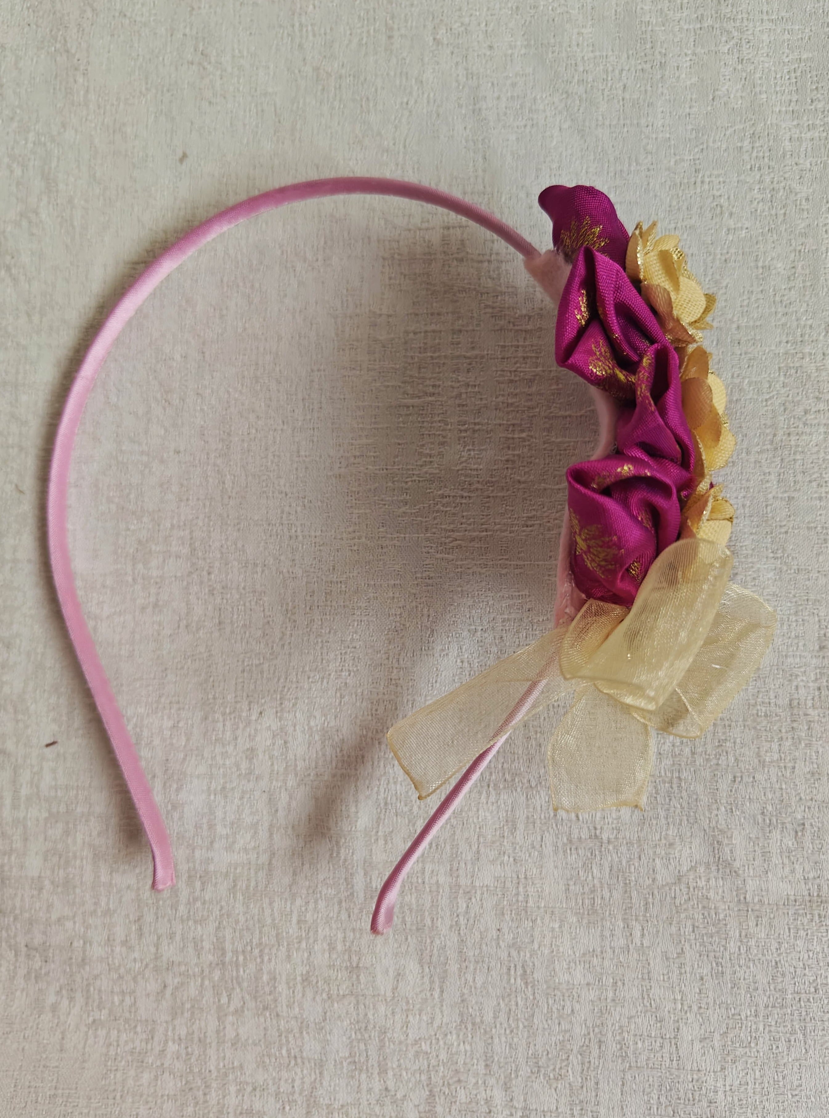 This Magenta flowers with violet headband&nbsp; for girls features delicate fabric flowers and is handcrafted with great care. It is ideal for girls over the age of 2 and makes a lovely addition to any outfit.