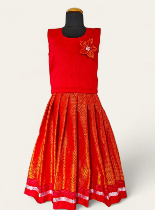 This creation features a handloom red khunn parkar with a striking green border, paired with a green raw silk sleeveless blouse. The blouse is adorned with handcrafted flower motifs, making it a perfect choice for girls.