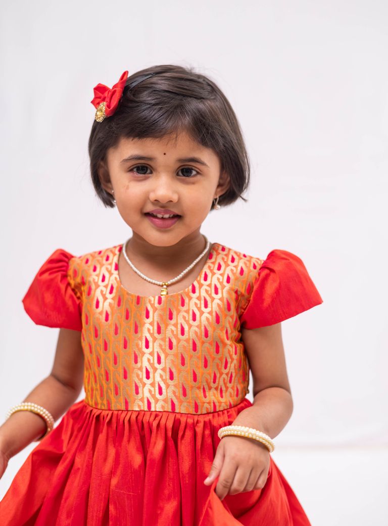 Orange banaras brocade with coral orange raw silk flared cap sleeved dress for Girls. Elevate any occasion with this unique piece.Let your princess be as comfortable as in her casuals with carefully designed and crafted Comfort Ethnic Wear by Soyara Ethnics. 