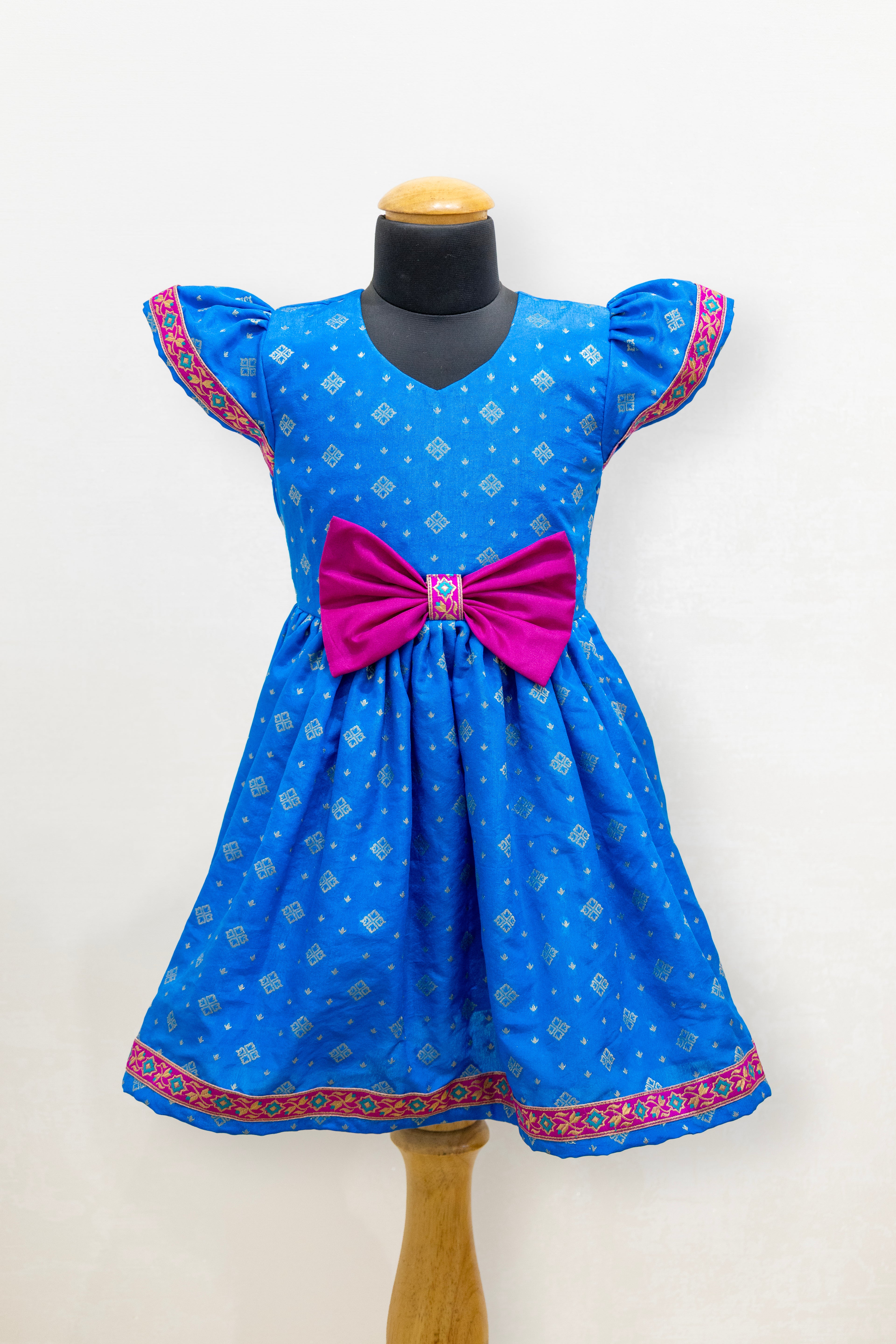 Blue brocade silk flared dress with puffed sleeves and contrast pink bow at the waistline for Girls