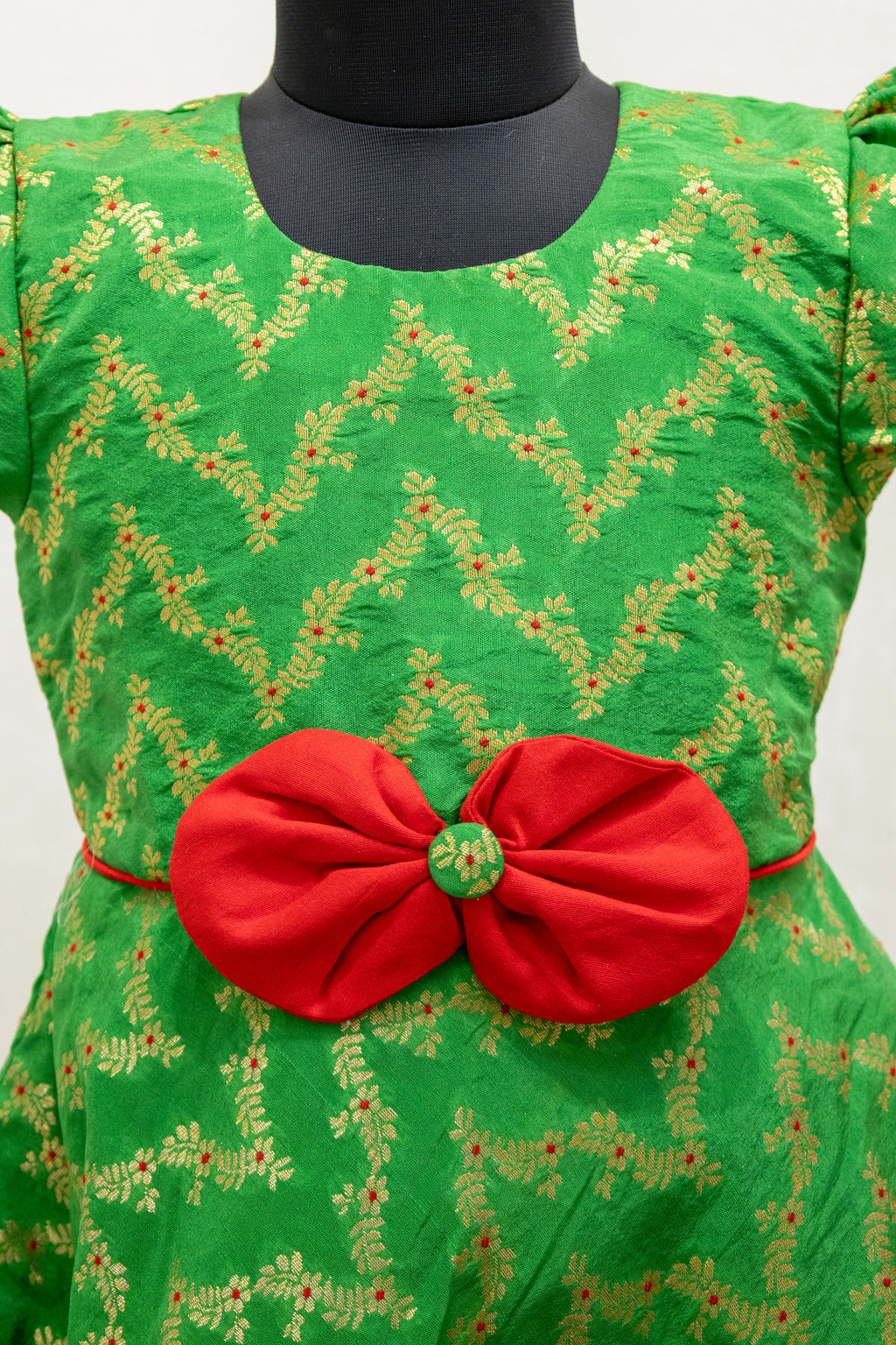 Green brocade silk flared dress with puffed sleeves and contrast red bow at the waistline for Girls