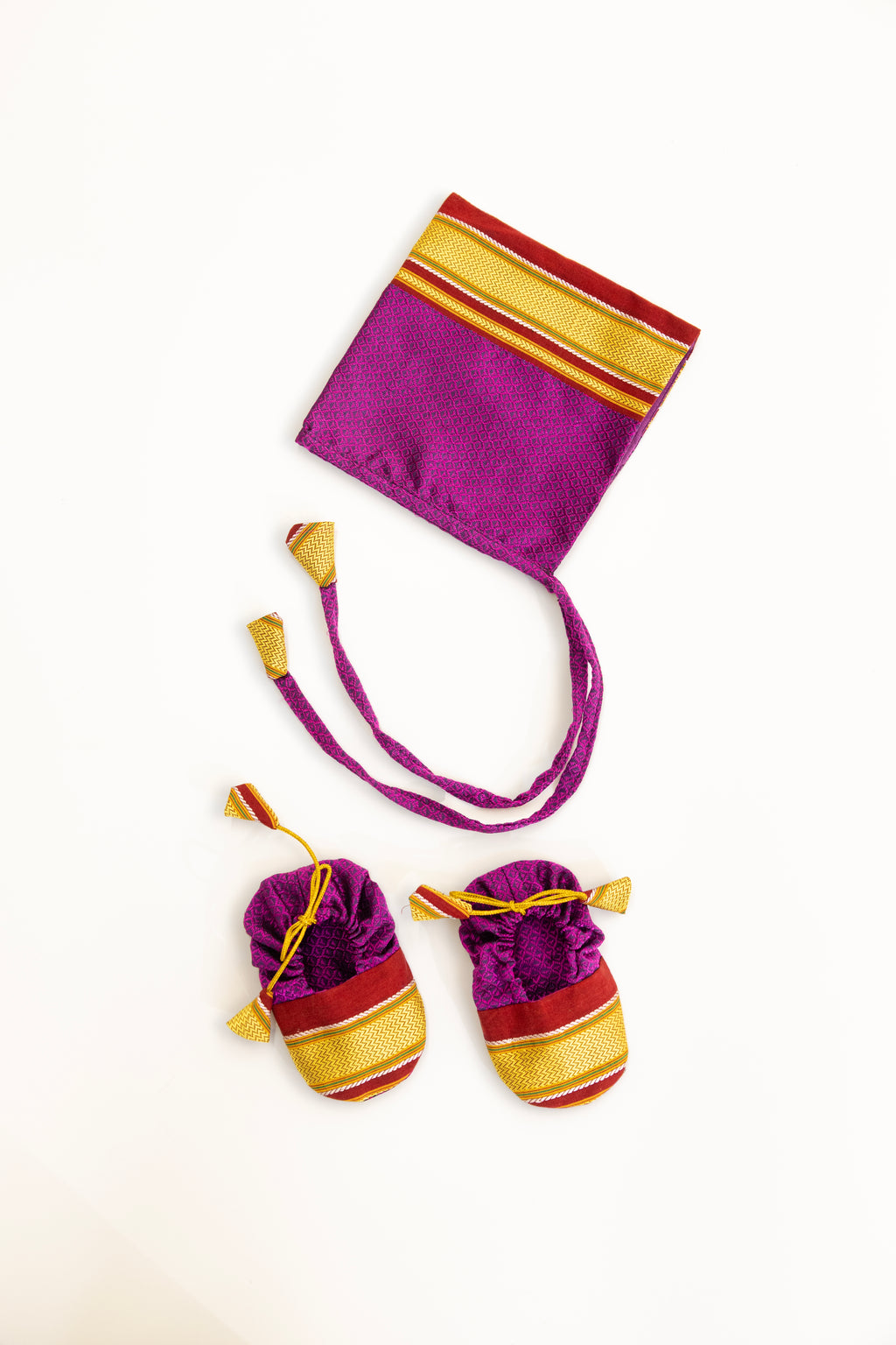 Purple handloom khunn with red border topda / topi/ bonnet with coordinated khunn booties set for NewBorn. Handcrafted accessories for Newborn are perfect add ons to any traditional attire of the baby.Designer baby mats,set of generic bloomers are other naming ceremony essentials.