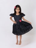 This girls’ flared dress features vibrant black taffeta silk, adorned with a handcrafted pink fabric flower motif and a chord waist belt. It is designed with elegant puffed cap sleeves for a refined finish.