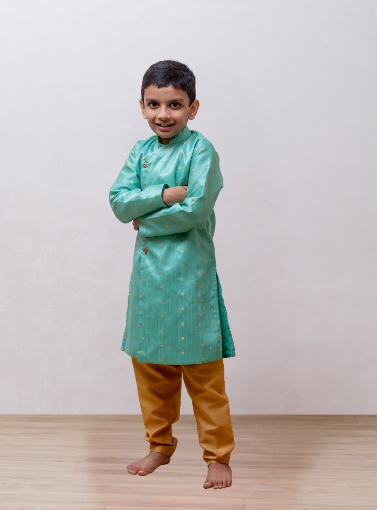 This boys' kurta features a pista mulberry silk fabric with a front open stand collar and distinctive stone-studded buttons. It is paired with a Golden Banglori silk salwar, and the kurta includes a comfortable cotton lining for added comfort.