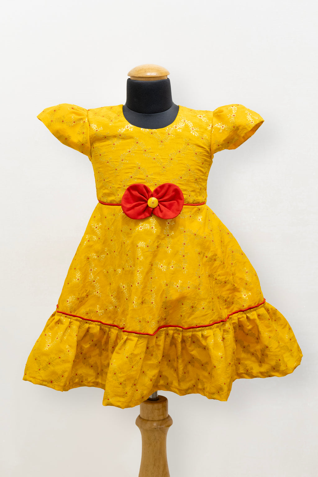 Yellow brocade silk flared dress with puffed sleeves and contrast red bow at the waistline for Girls
