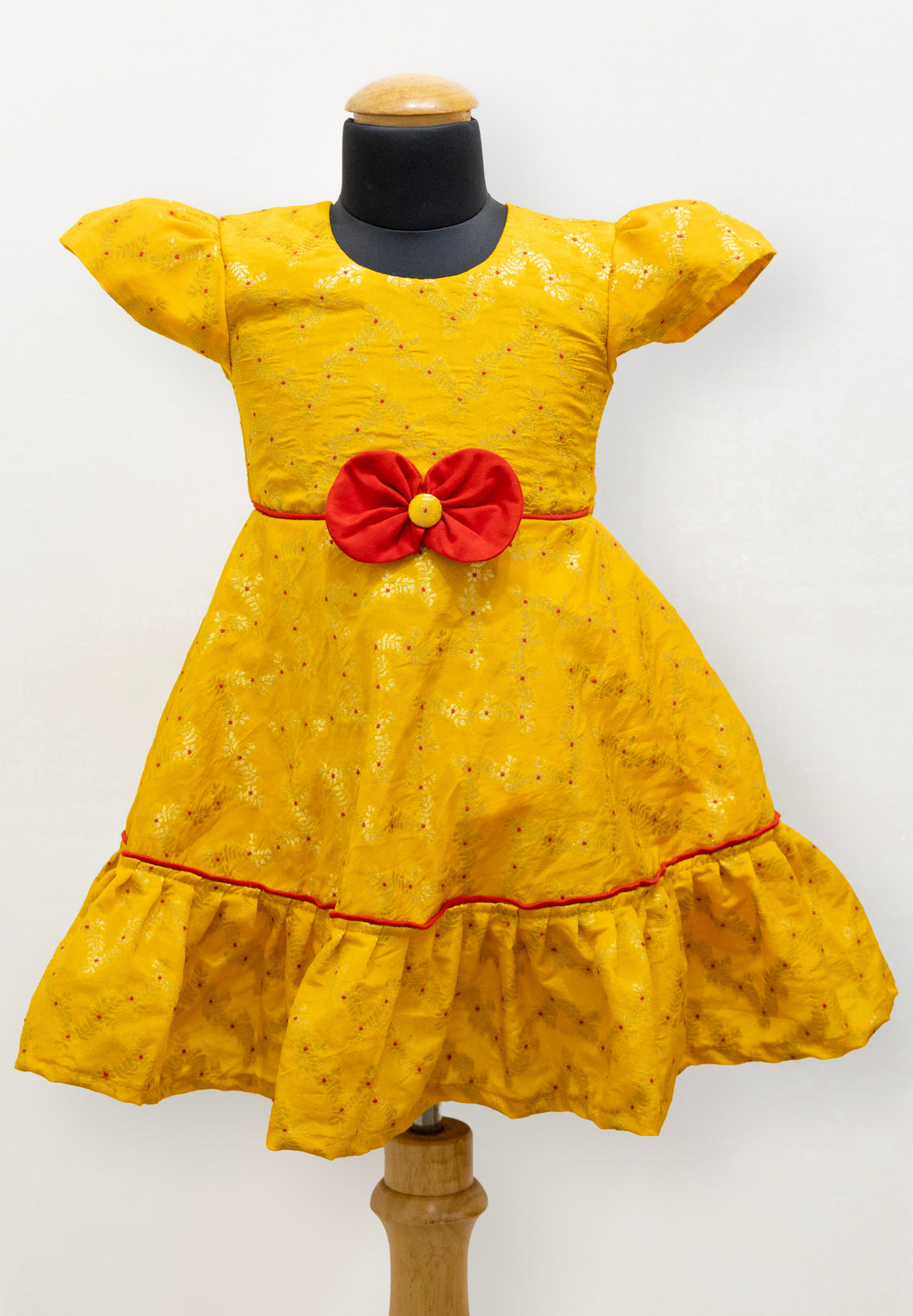 Yellow brocade silk flared dress with puffed sleeves and contrast red bow at the waistline for Girls