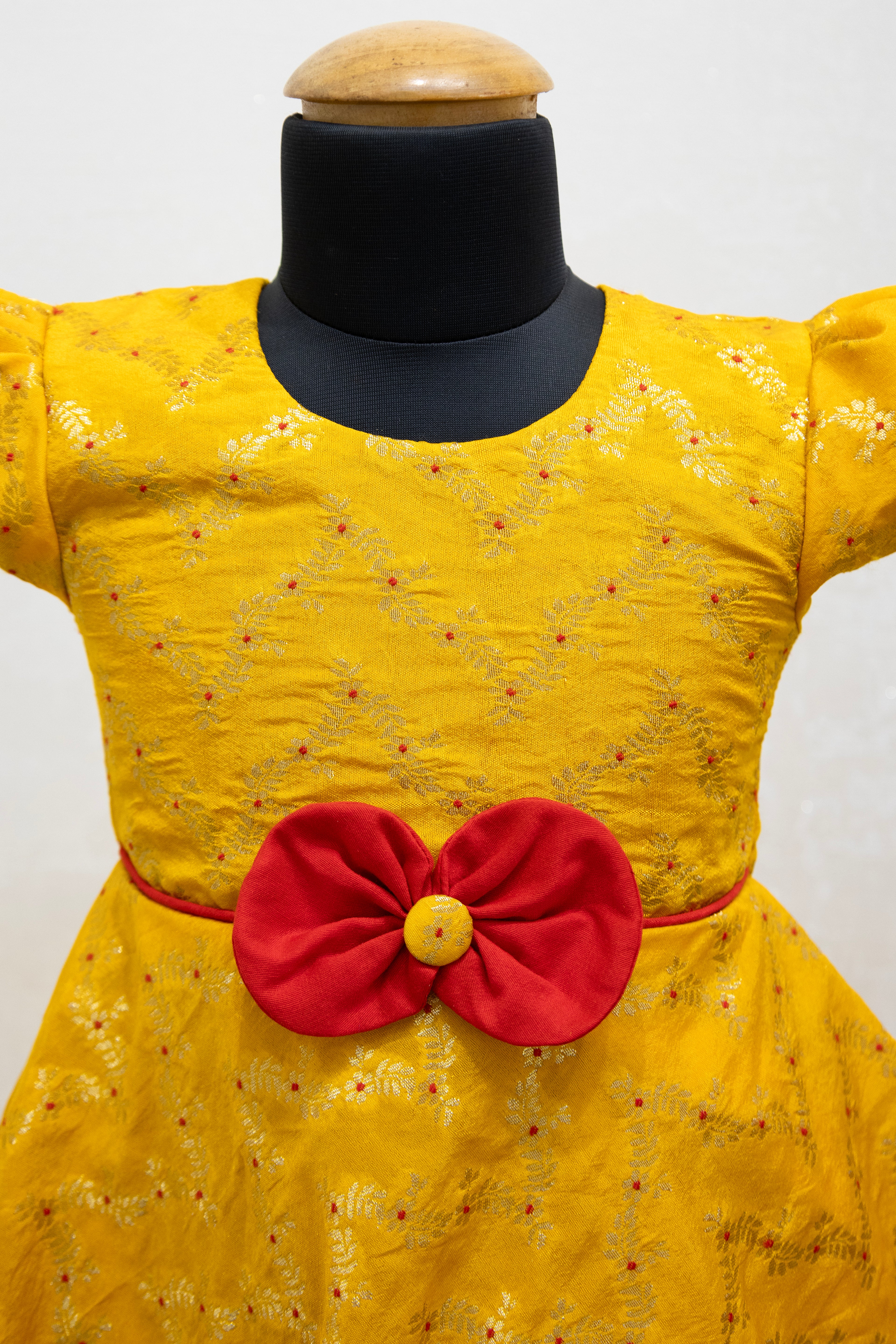Yellow brocade silk flared dress with puffed sleeves and contrast red bow at the waistline for Girls