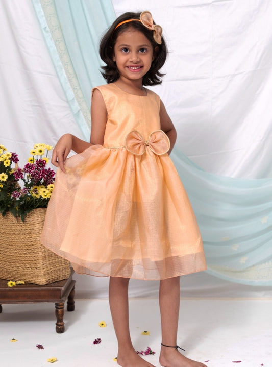 Peach tissue kotta silk sleeveless flared dress with statement embellished bow for Girl.Peach tissue kotta fabric has a subtle shimmer all over yet maintains a soft touch.The statement bow is highlighted with golden chord and waist belt has cute flowers detailing at the ends.